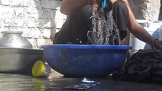 Indian stepsister is preparing to take a bath while washing clothes in the open courtyard of the house